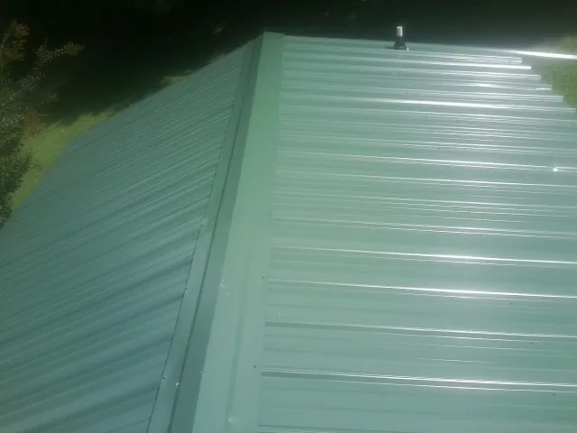 New green metal panels meeting at the ridge of a roof — Flat Roof Repair work by our crew in Macon