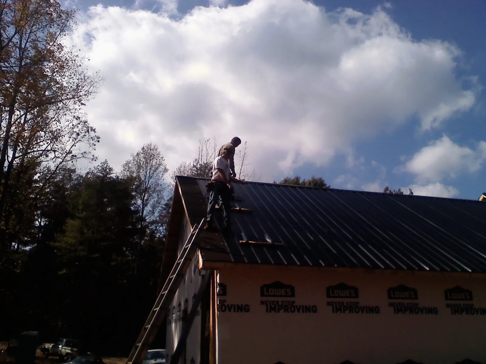 Roofer fastening dark metal panels high against a cloudy sky, from a Roof Inspection job in Macon