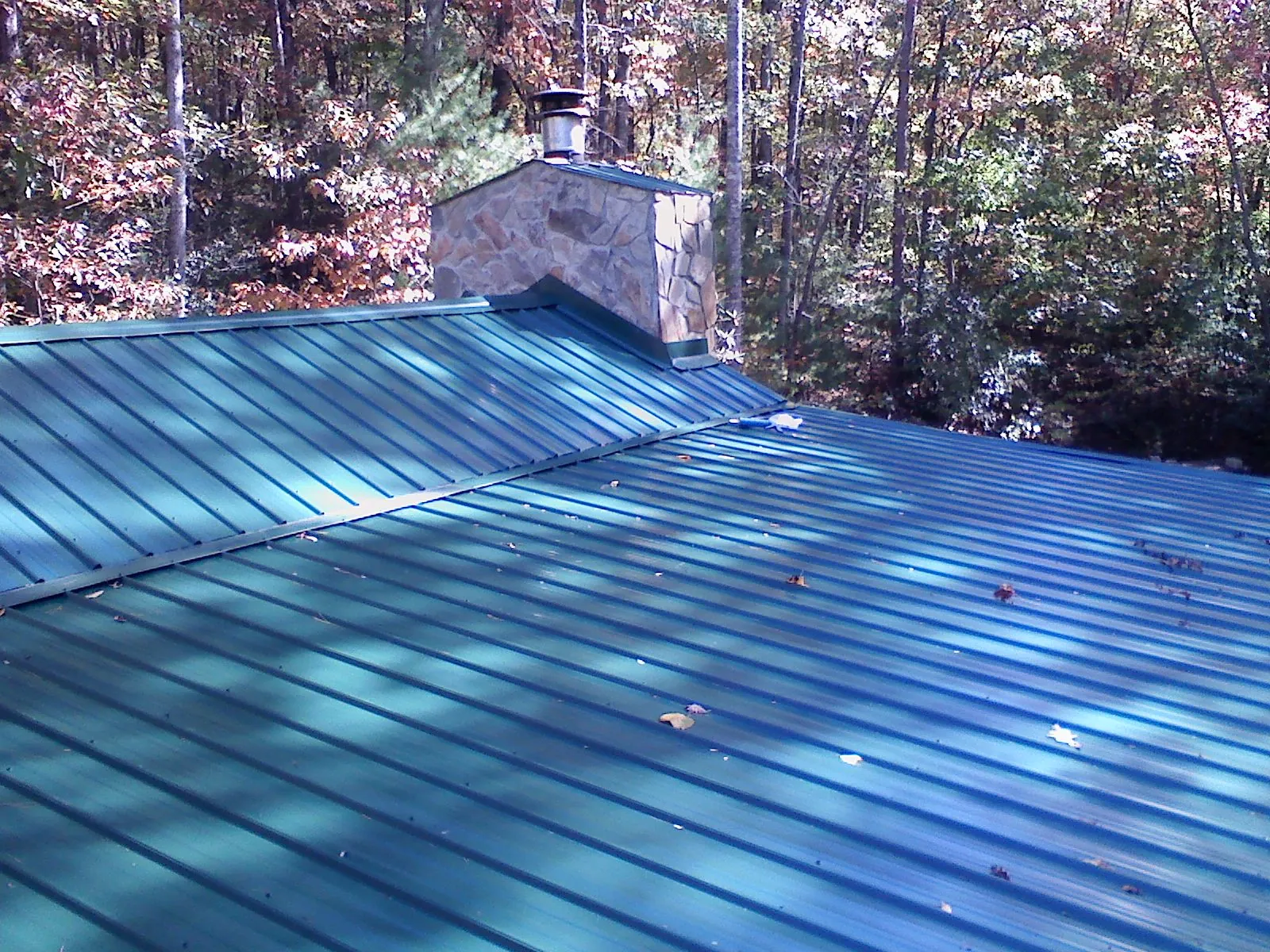 New green metal roof and stone chimney surrounded by autumn woods in Macon