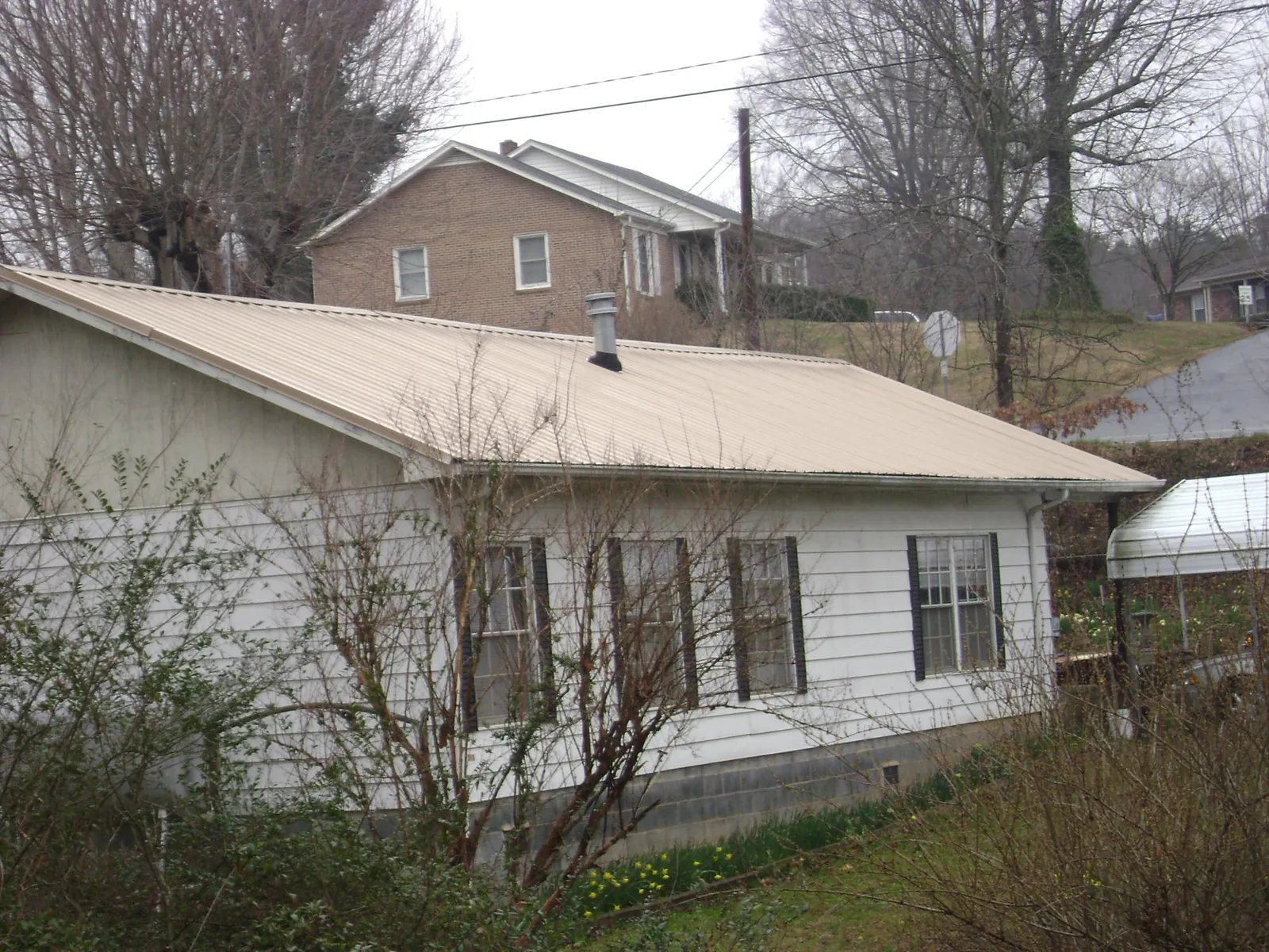 Tan metal roof on a white sided house set into a hillside — Commercial Roofing by Roofing Brothers in Macon